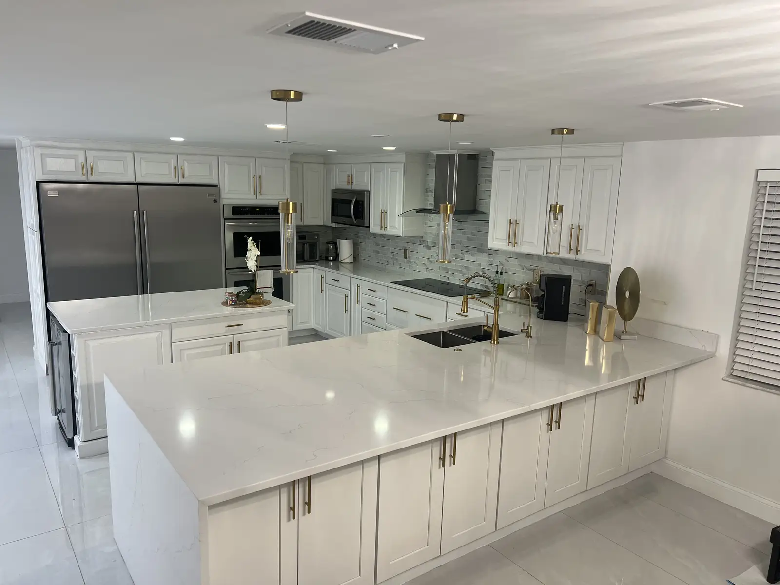 White kitchen remodel with quartz peninsula and gold hardware by Venet LLC in Tampa Bay, Florida