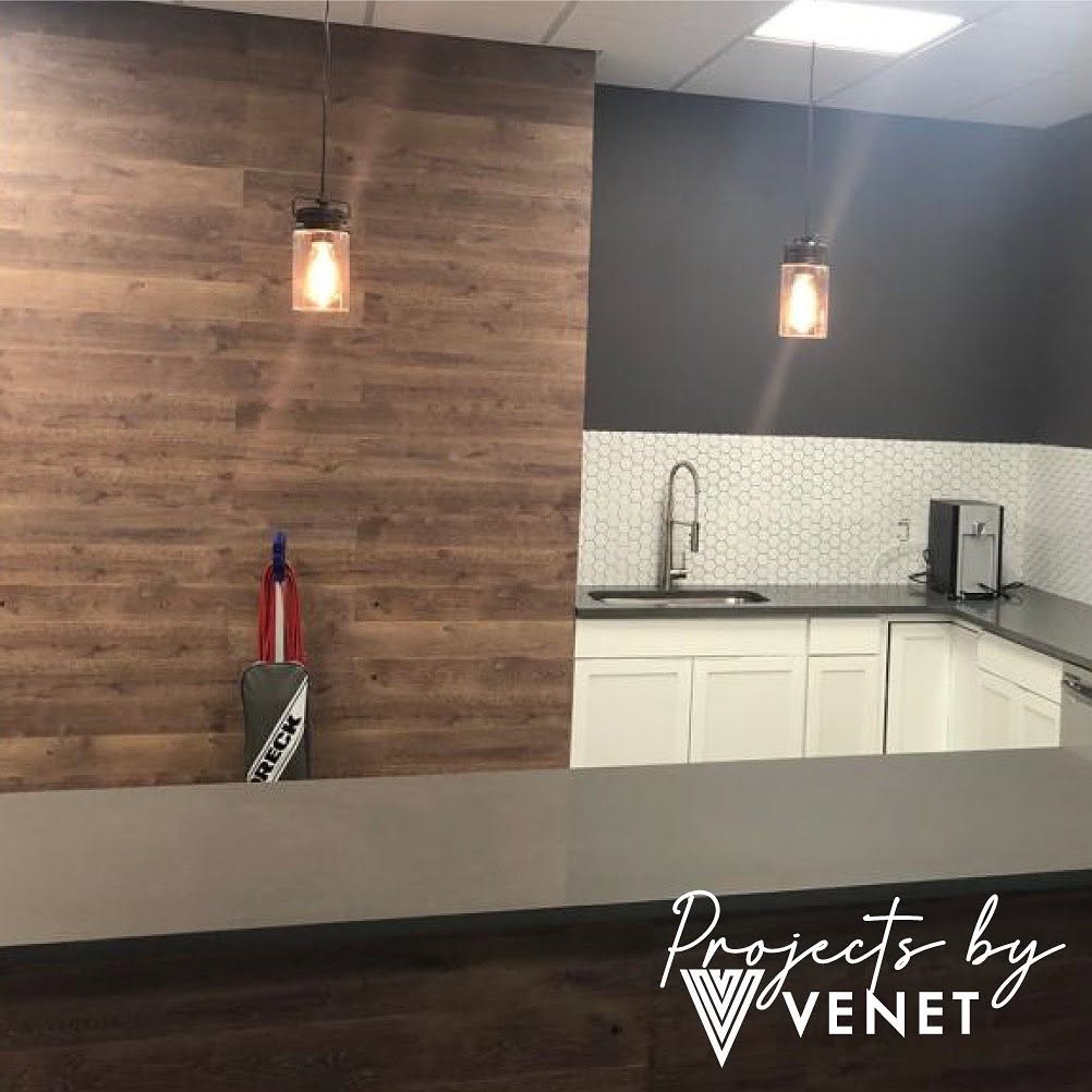 Finished commercial break room installation with gray countertop, white cabinetry and wood accent wall by Venet LLC in Tampa Bay